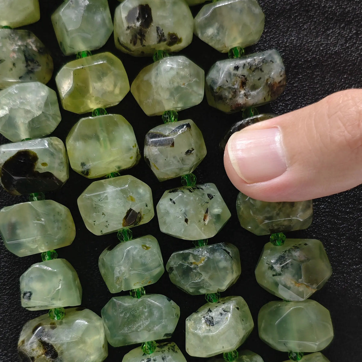 Finger pointing to a large natural prehnite freeform faceted bead displaying natural earthy inclusions and facets