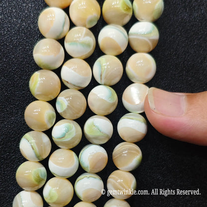 Finger inspecting strands of natural green swirl shell round beads displaying smooth glossy polish
