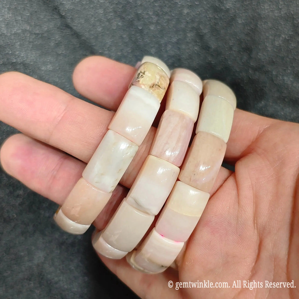 Hand holding three pastel pink opal curved segment stretch bracelets showing polished curved porcelain surfaces