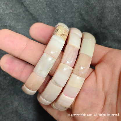 Hand holding three pastel pink opal curved segment stretch bracelets showing polished curved porcelain surfaces