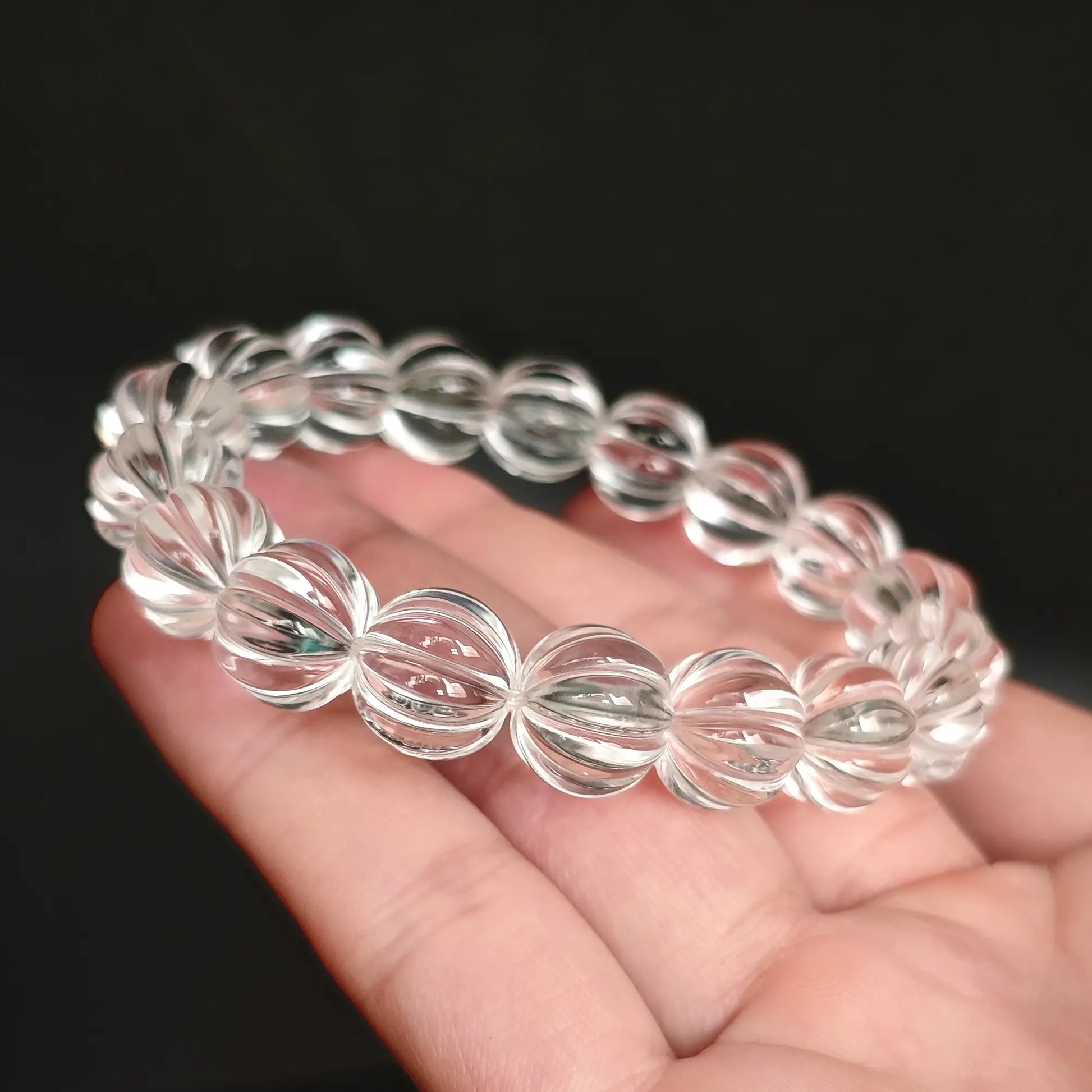 Hand displaying clear quartz pumpkin beads in extended line, revealing precise faceting, natural inclusions, and crystal clarity