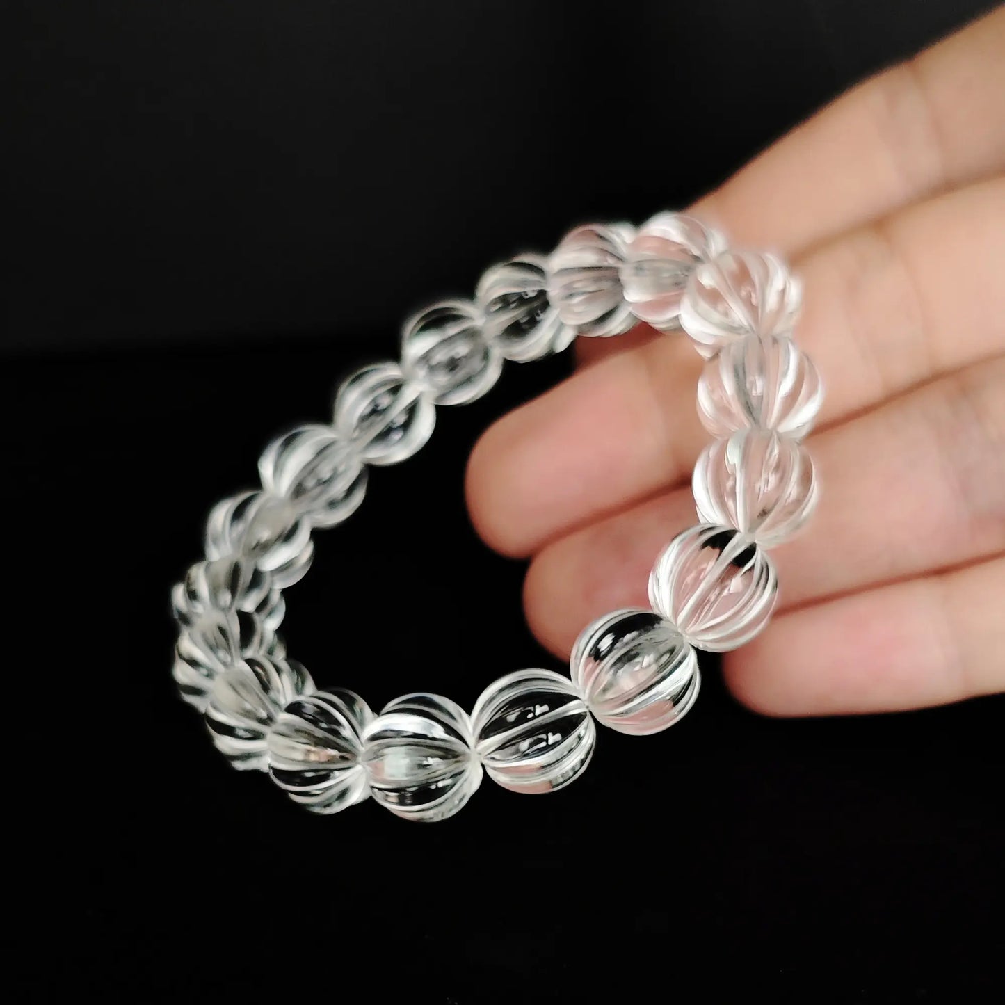 Hand holding clear quartz bracelet formed into a circle, emphasizing geometric facets and internal light play through transparent crystal