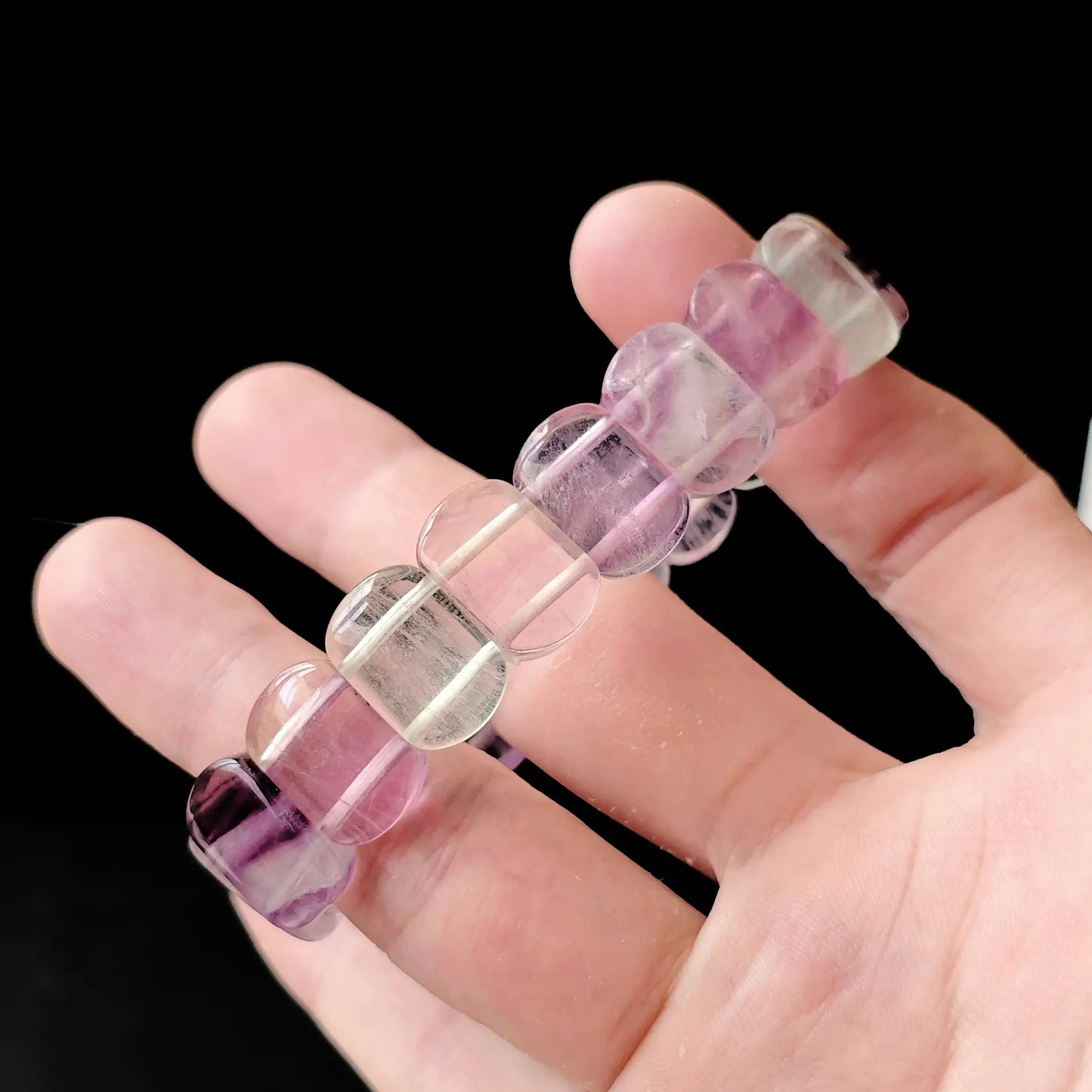 Side view of fluorite oval beads held between fingers, emphasizing elongated shape and light refraction through translucent stone