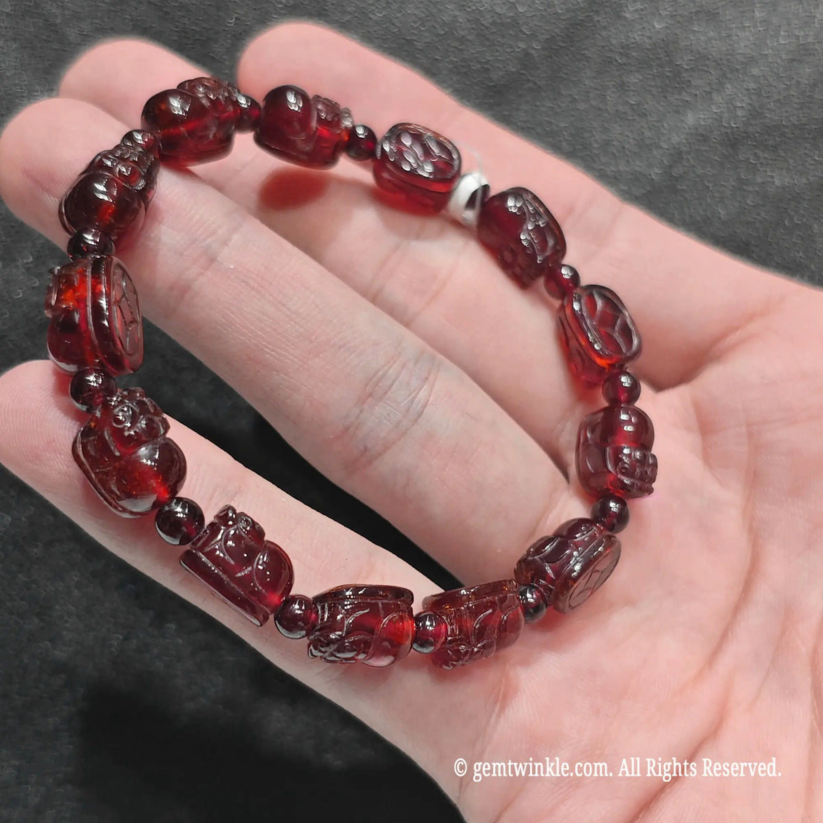 Top view of garnet pi yao carving charm strand showing intricate miniature mythical creature beads on hand