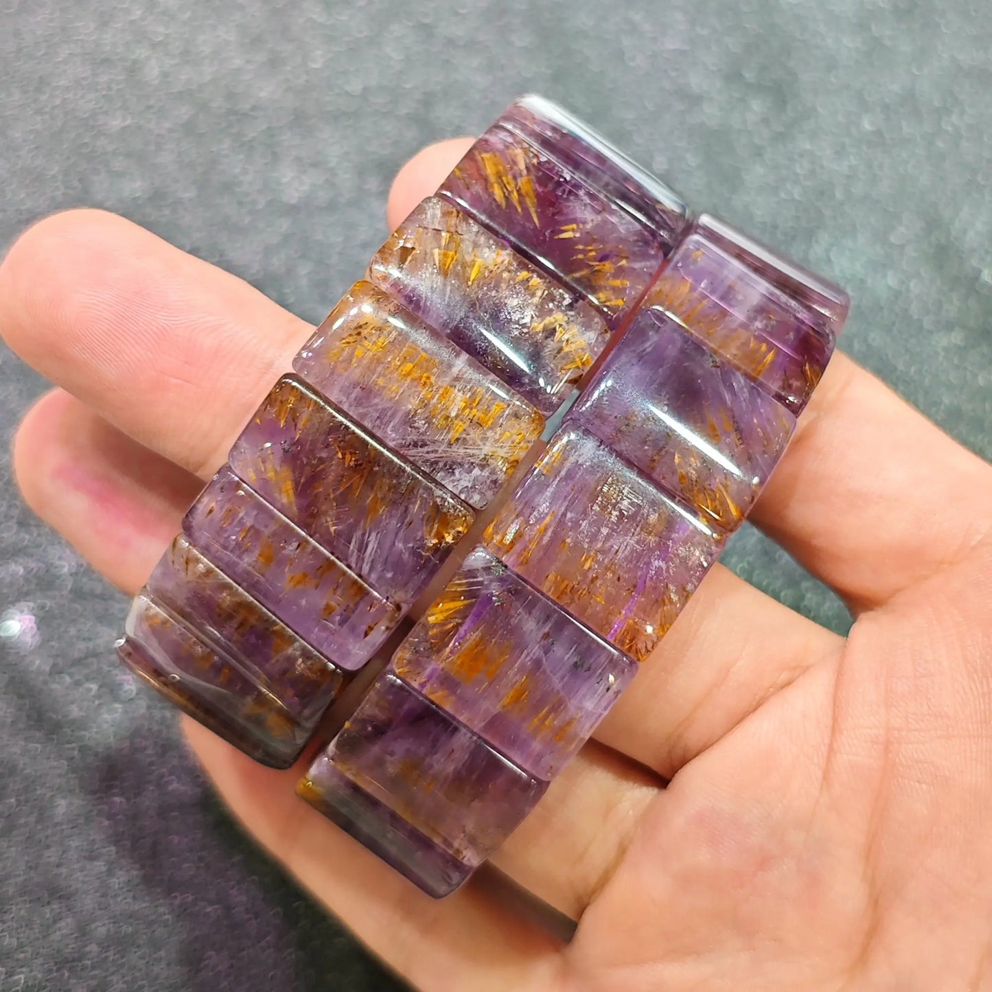 Hand holding two natural black gold super seven crystal bangles comparing rutile density and violet mineral tones