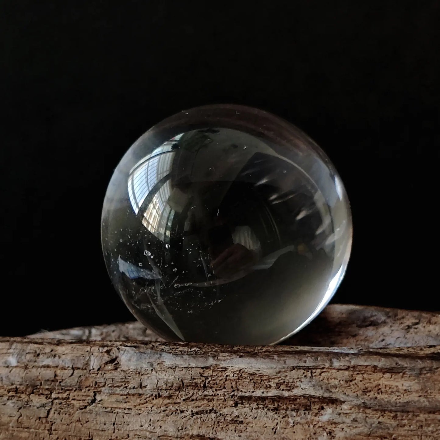 Natural clear quartz sphere (~2cm), highly transparent with glassy luster, resting on a small resin base; premium crystal desk decor for mindful spaces