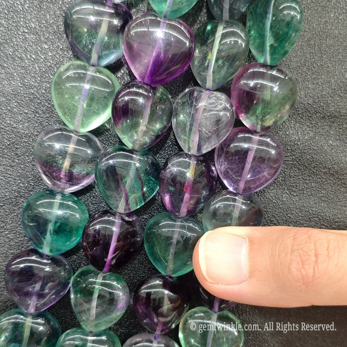 Multiple strands of rainbow fluorite heart shaped beads aligned showing pre-drilled vertical holes and pastel color spectrum