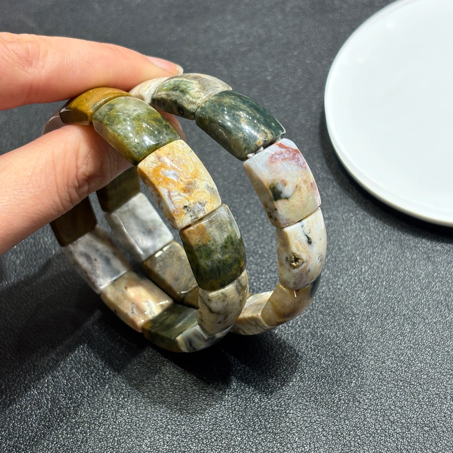 Hand holding two natural ocean jasper square bead bracelets; shows texture, weight, and how they layer for personal expression