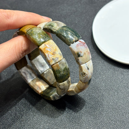 Hand holding two natural ocean jasper square bead bracelets; shows texture, weight, and how they layer for personal expression