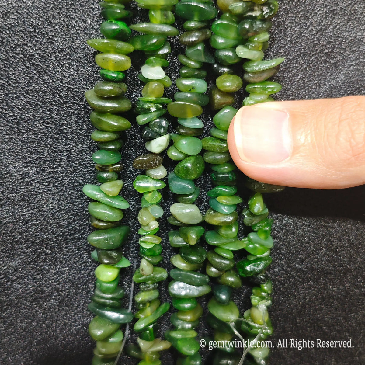 Close up hand holding natural hotan nephrite jade stone chips displaying polished green surfaces and fine drill holes