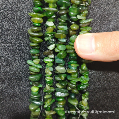 Close up hand holding natural hotan nephrite jade stone chips displaying polished green surfaces and fine drill holes