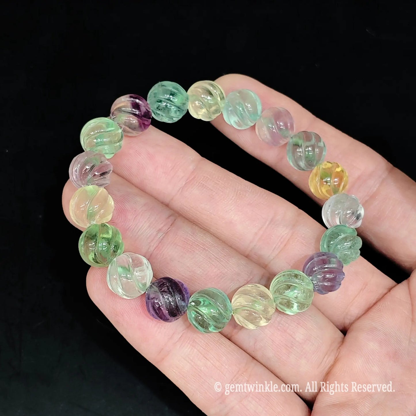 Carved fluorite melon bead bracelet held in hand under lighting showing translucent crystal texture and internal ice veils