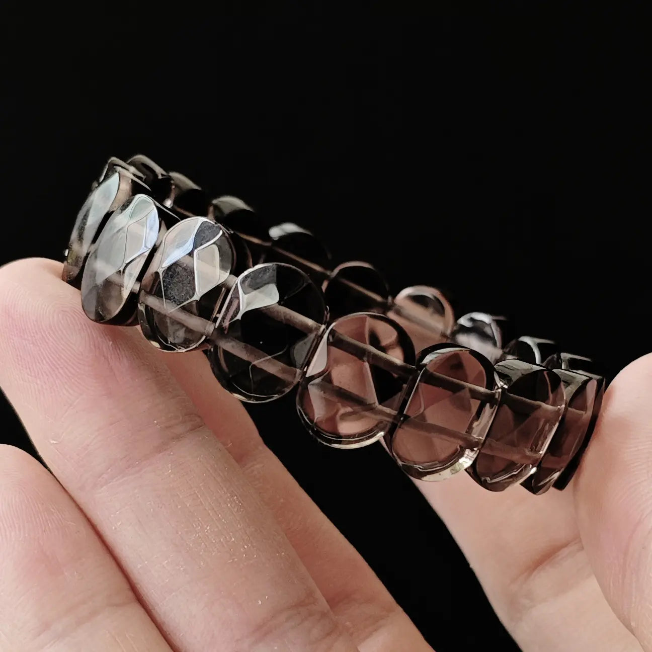 Hand holding ice-grade black obsidian bracelet at angle to demonstrate light passing through beads—proof of high-quality transparent obsidian, not cloudy or opaque