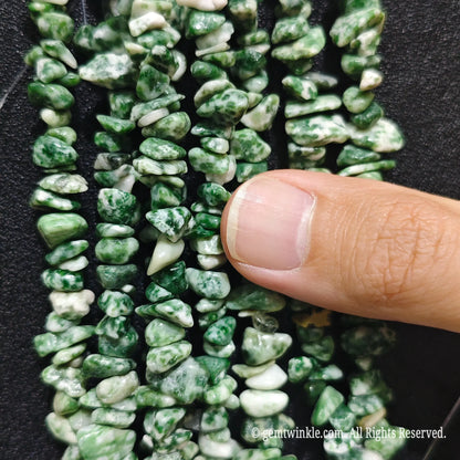 Fingers holding natural green spot kiwi jasper gemstone chip beads on black background