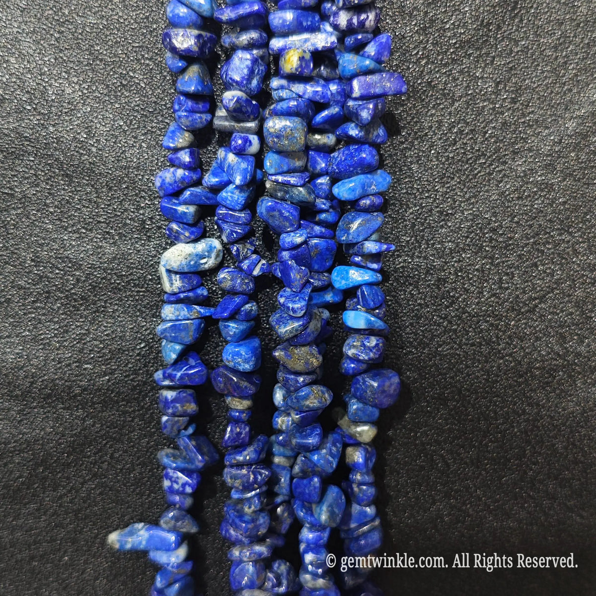 Close up hand holding natural lapis lazuli stone chips displaying polished deep blue surfaces and fine drill holes