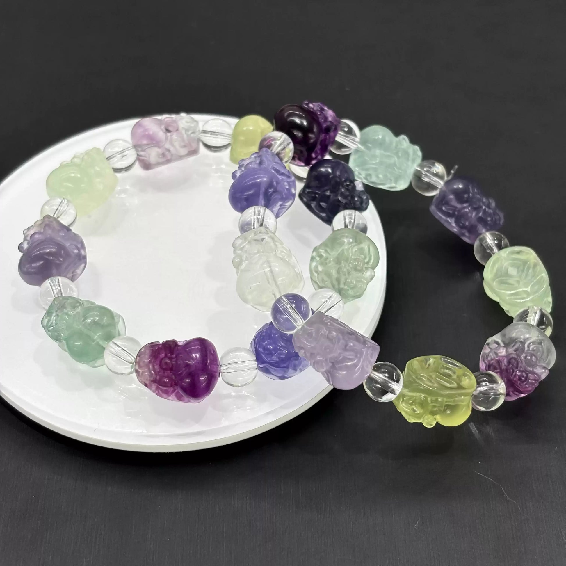 Two fluorite Pi Xiu bracelets styled together on white ceramic dish—showcasing natural color variation and smooth carving