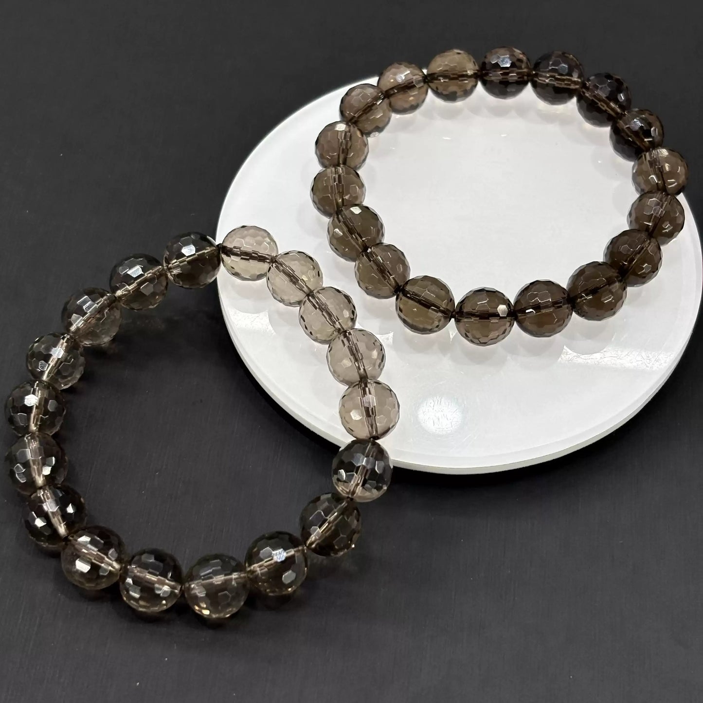Two smoky quartz faceted bracelets styled on white ceramic dish—showcasing depth of gray tones and precise facet patterns