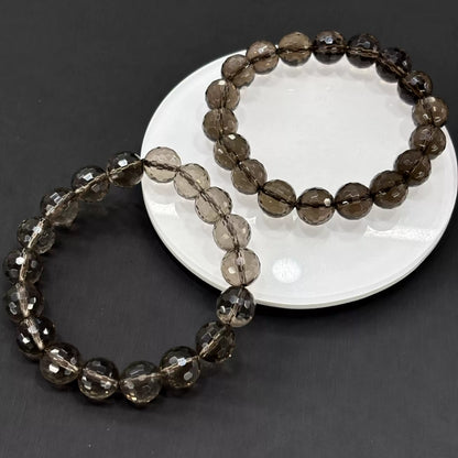 Two smoky quartz faceted bracelets styled on white ceramic dish—showcasing depth of gray tones and precise facet patterns