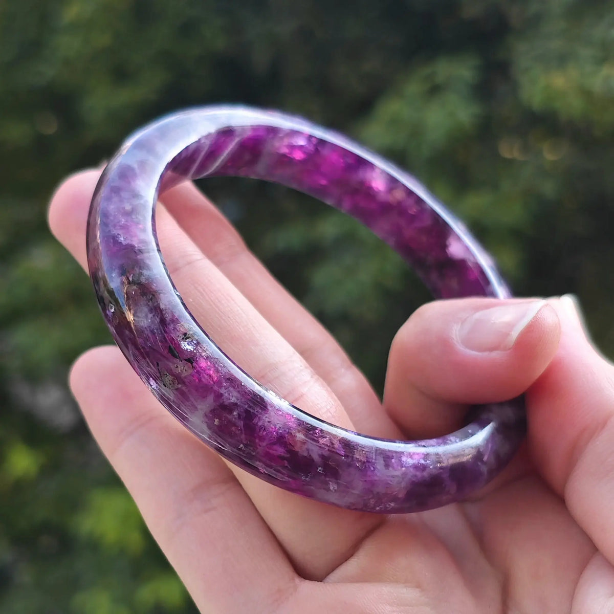 Hand displaying natural purple lepidolite bangle highlighting vibrant color distribution and mirror polish