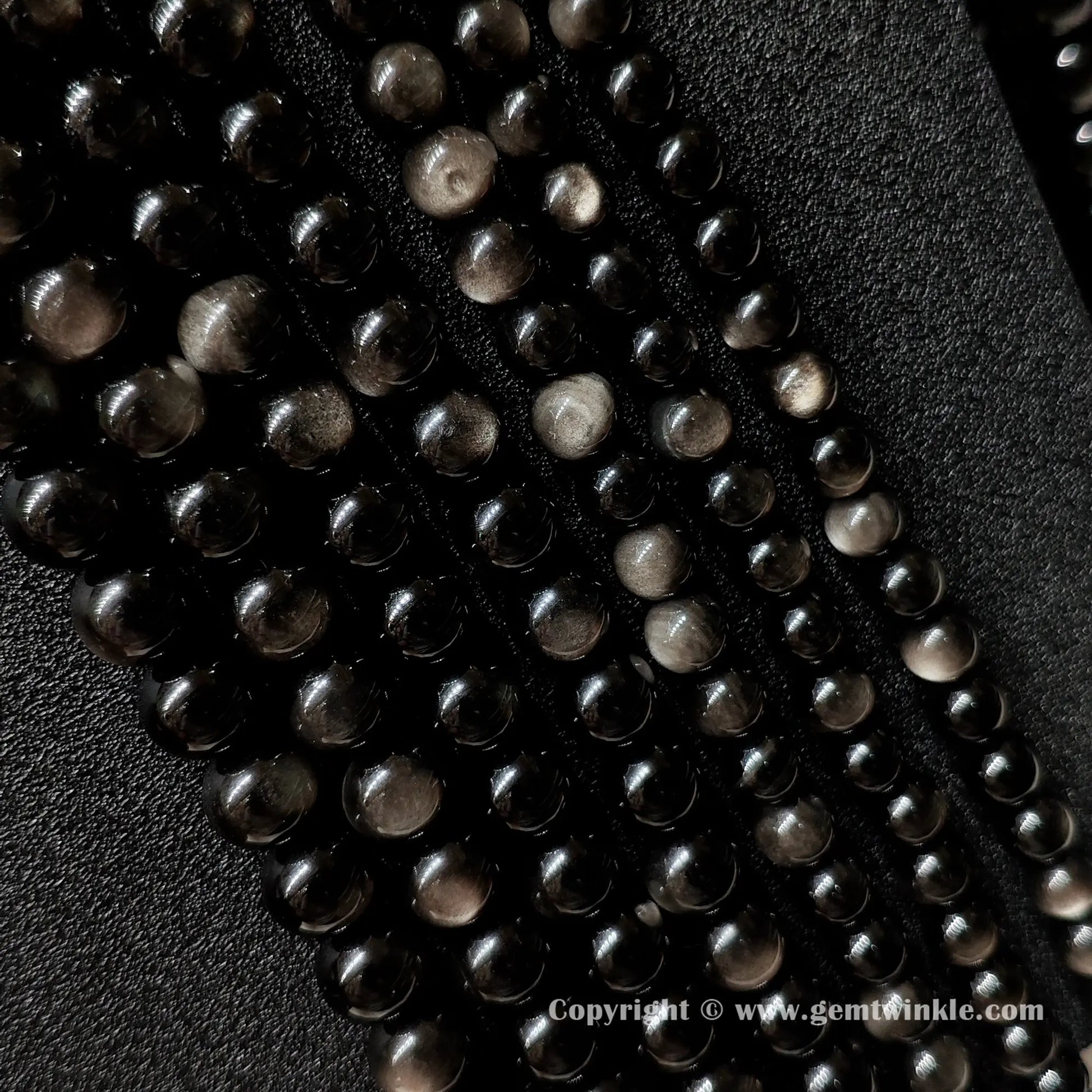Parallel rows of Grade A silver sheen obsidian round bead strands demonstrating size range from 6mm up to 16mm
