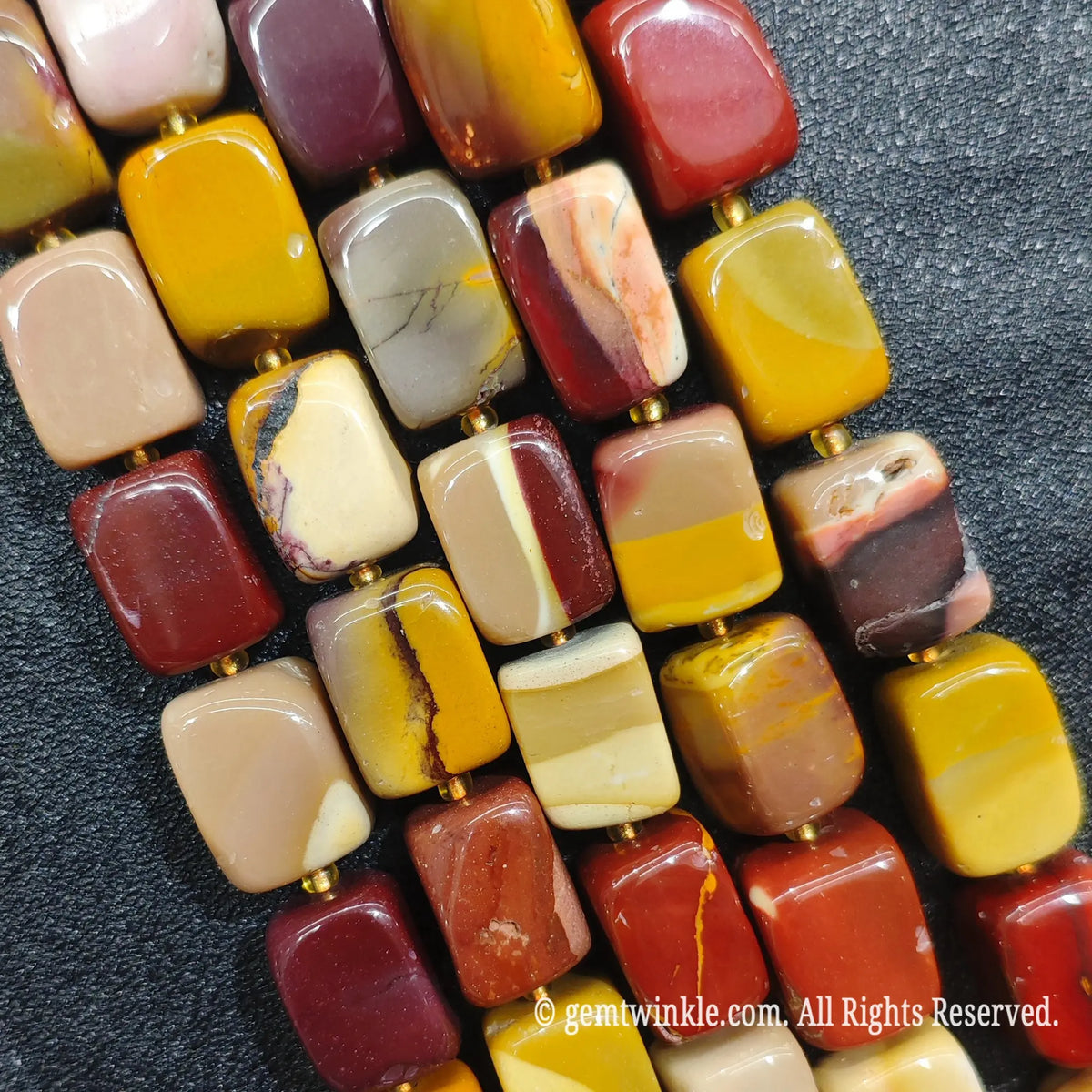 Hand holding strands of Mookaite Jasper rectangular beads showcasing polished surface and natural swirl patterns