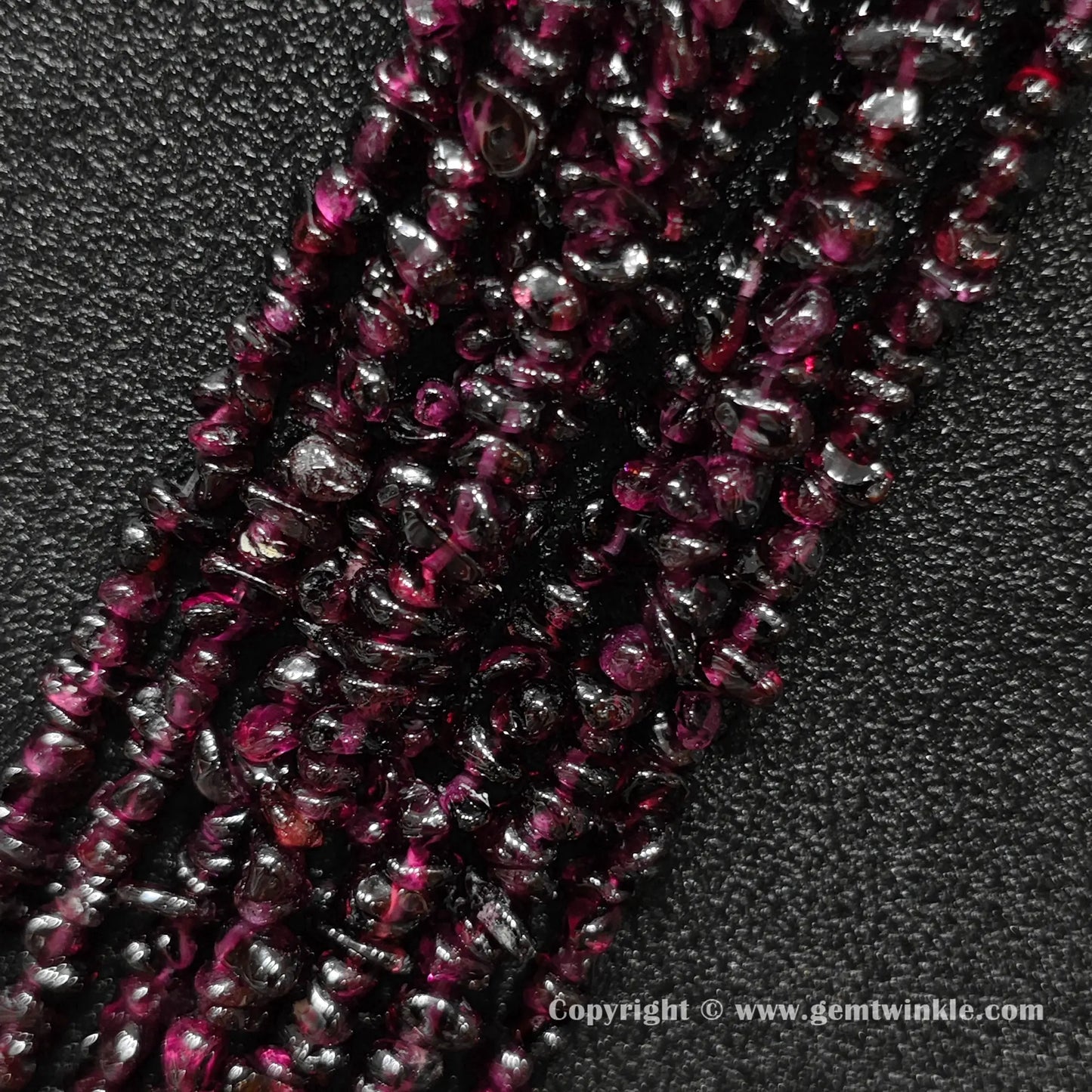 Angled view of tumbled wine red garnet freeform chip gemstone strands