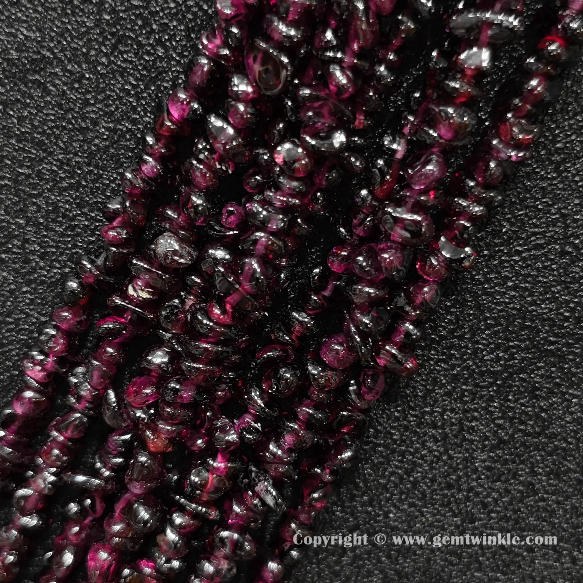 Angled view of tumbled wine red garnet freeform chip gemstone strands