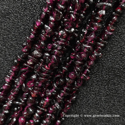 Angled view of tumbled wine red garnet freeform chip gemstone strands