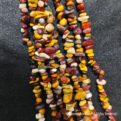 Close up hand holding natural mookite stone chips displaying polished yellow and amber surfaces with fine drill holes