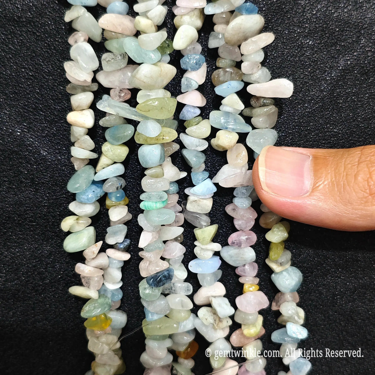 Fingers holding natural multi-color morganite gemstone chip beads on black background