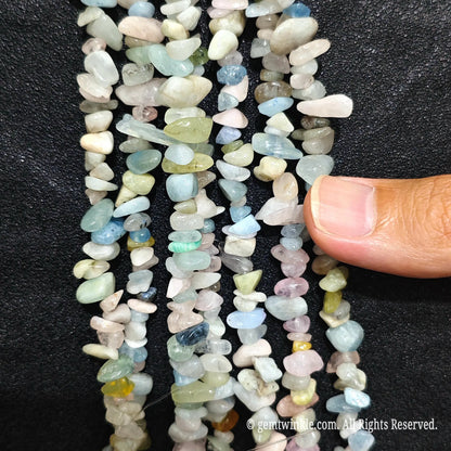 Fingers holding natural multi-color morganite gemstone chip beads on black background
