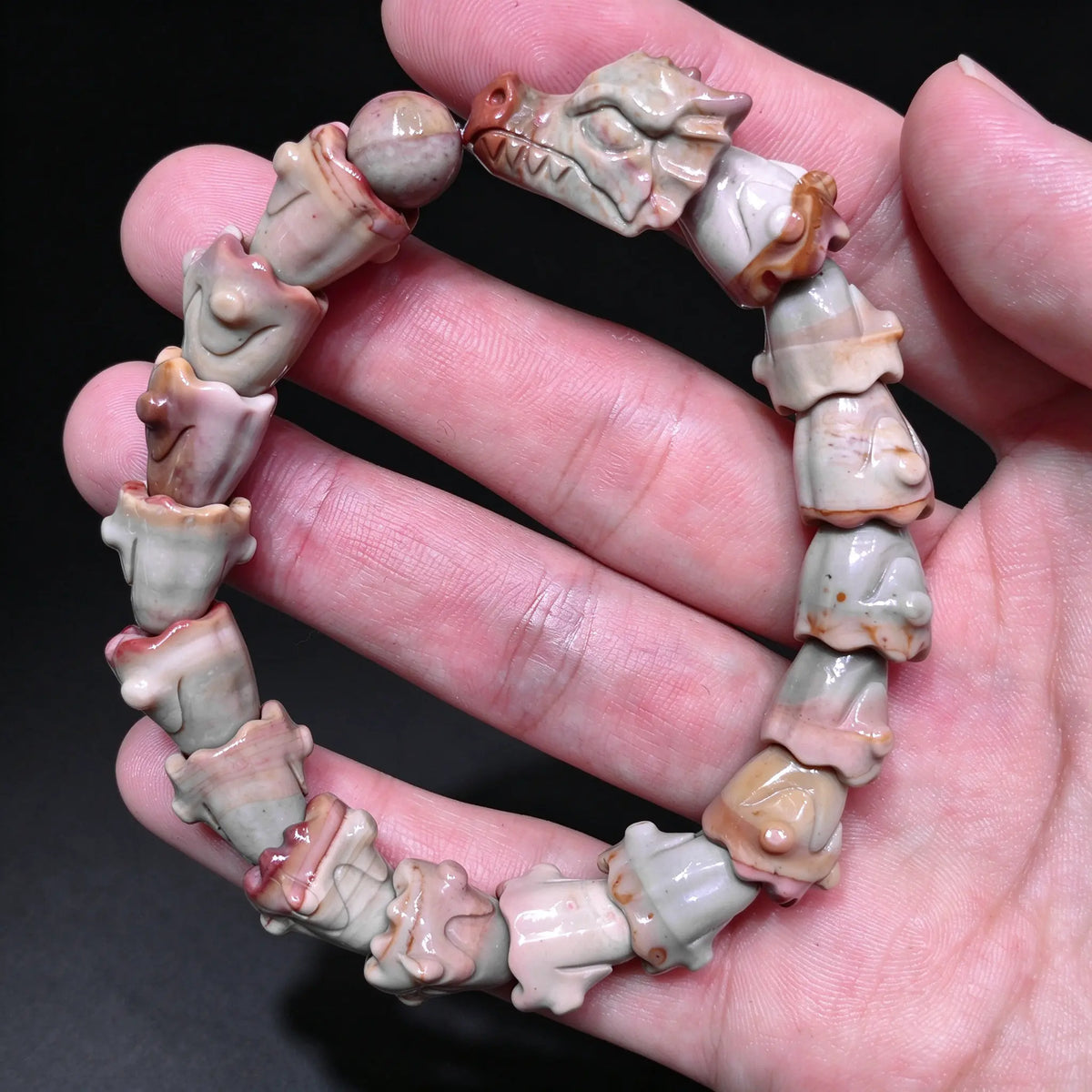 Hand holding a natural multi color Alxa agate dragon spine carved stretch bracelet showing detailed dragon head centerpiece