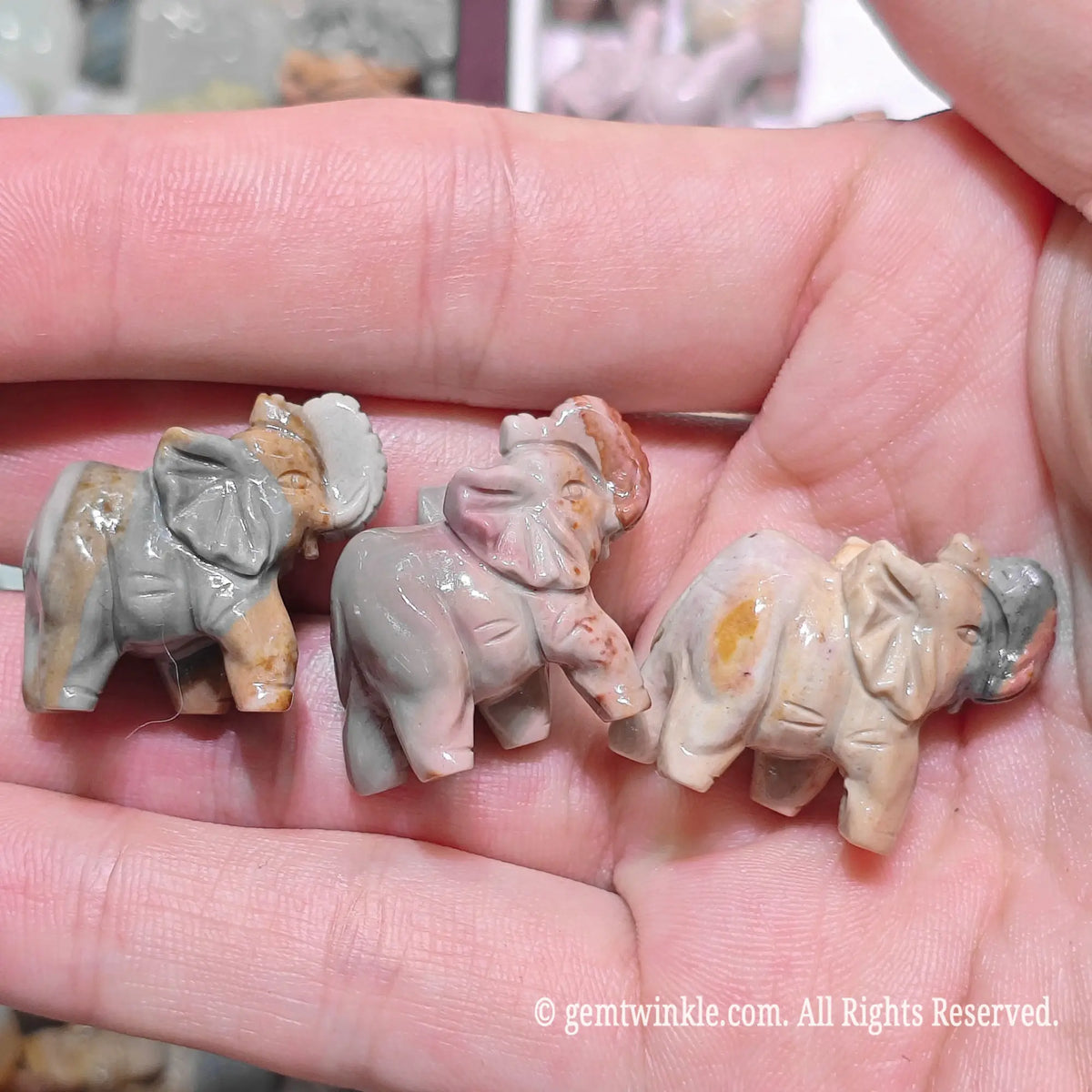 Close up view of natural multi color Alxa agate mini elephant statues resting on hand highlighting polished finish