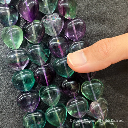 Detail view of natural rainbow fluorite heart beads highlighting light reflecting polished surfaces and translucent crystal depth