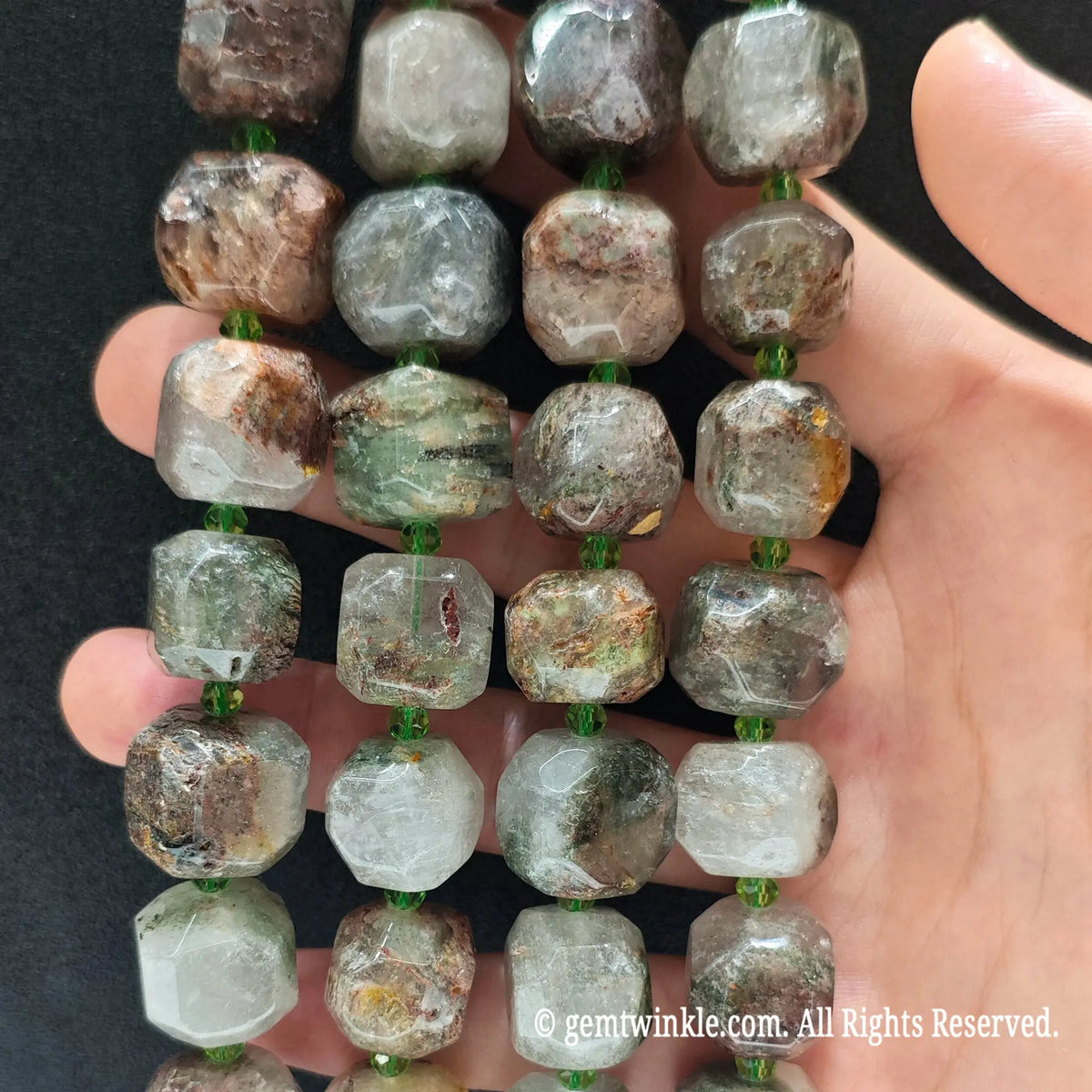 Hand holding three strands of natural green phantom quartz faceted square cube beads showing multi-color mineral layers