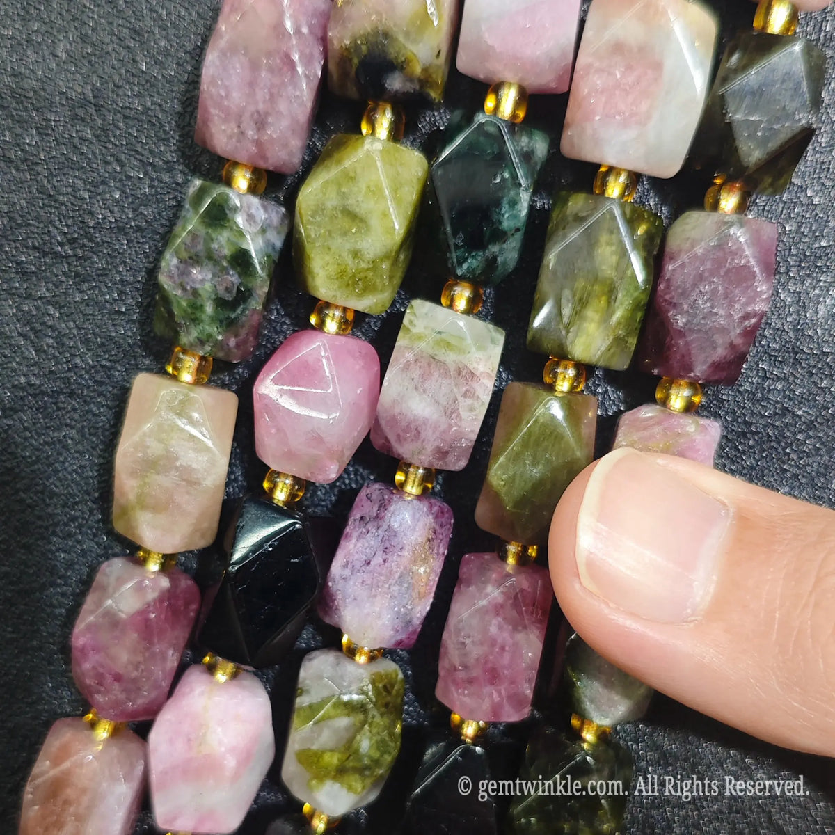 Hand holding four strands of natural candy tourmaline faceted freeform beads showing vibrant pink and green crystal colors