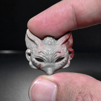 Fingers holding a small natural Alxa agate fox mask carved mini statue with gray body and terracotta red ear accents