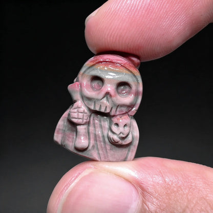 Fingers holding a small natural Alxa agate Grim Reaper carved mini statue in pink and gray natural color banding