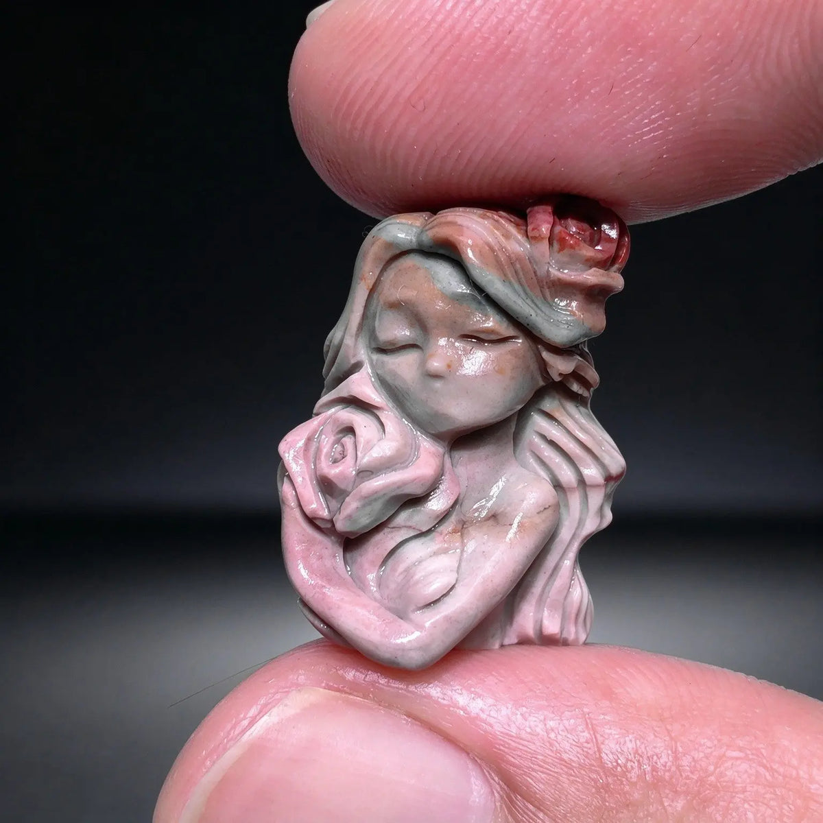 Fingers holding a small natural Alxa agate rose maiden carved mini statue showing pink rose detail and smooth polish