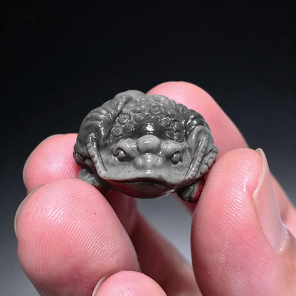 Fingers holding a small natural Alxa agate three-legged money toad carved mini statue in slate gray showing smooth polish