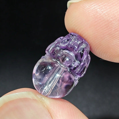 Fingers holding a natural purple amethyst Pixiu carved focal bead showing internal ice veining and polished surface