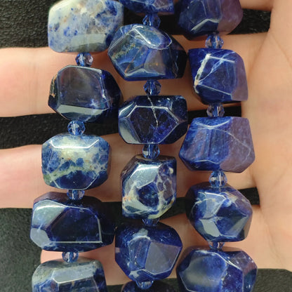 Strands of natural blue sodalite freeform faceted beads with white calcite veining displayed on dark background