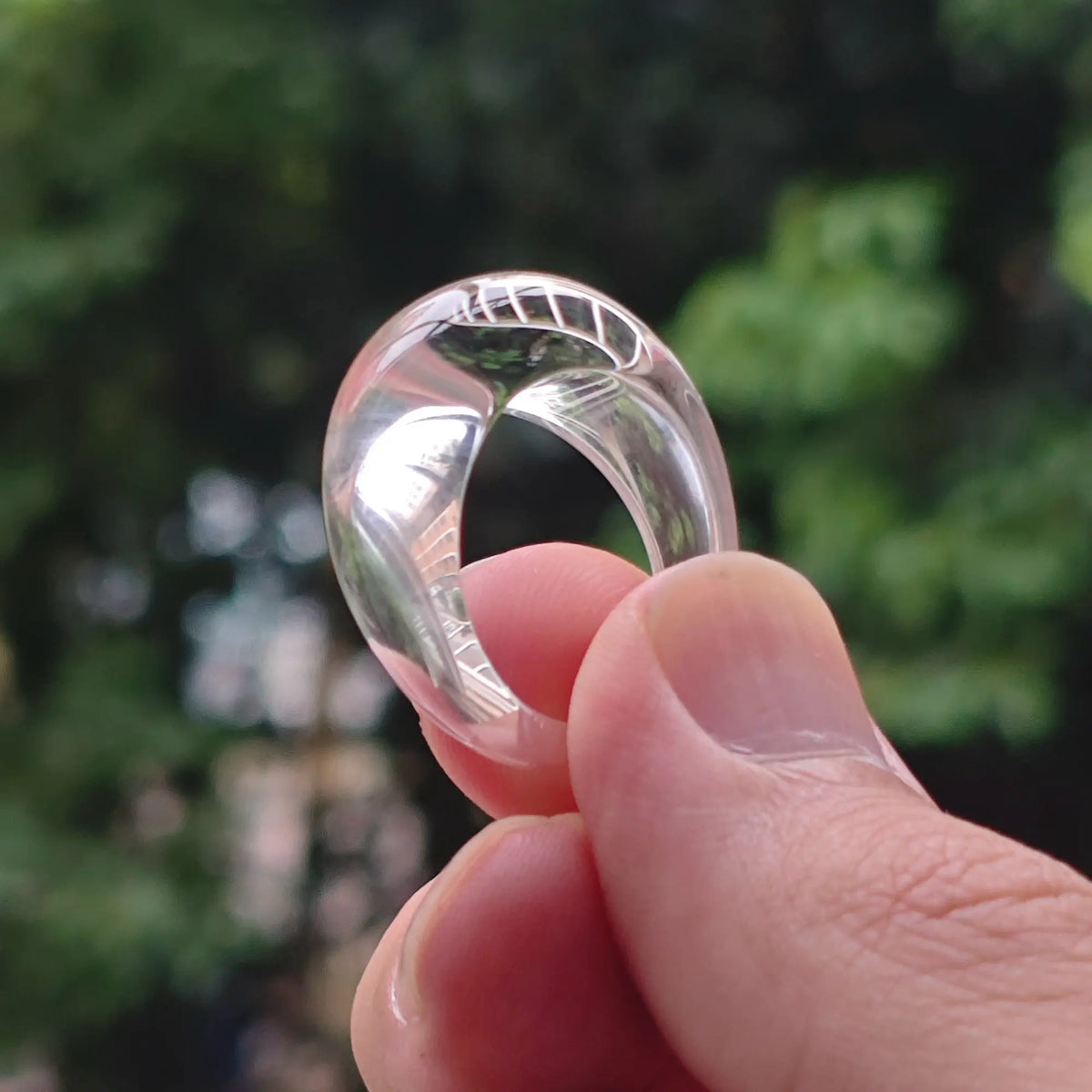 Solid carved natural clear quartz ring held in fingers showing high transparency and mirror polish