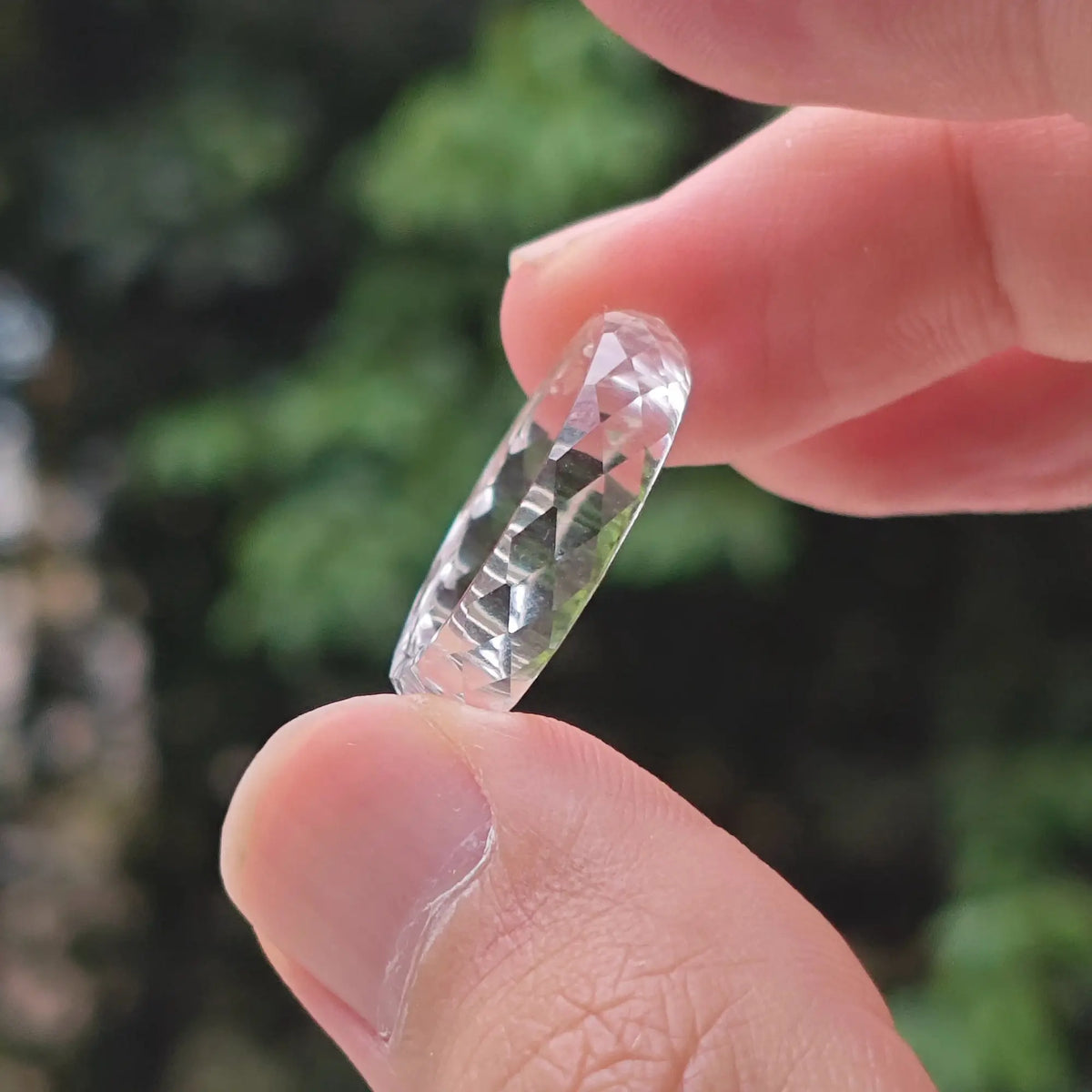 Solid carved diamond-cut natural clear quartz ring held in fingers showing sparkling micro facets and mirror polish