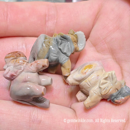 Hand holding small Alxa agate elephant figurines from side and bottom perspective showing precision carved shape