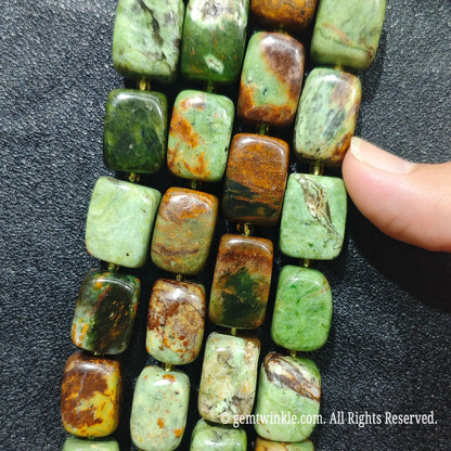 Close up view of natural green jasper pillar beads aligned on strands showing natural earth tone variations