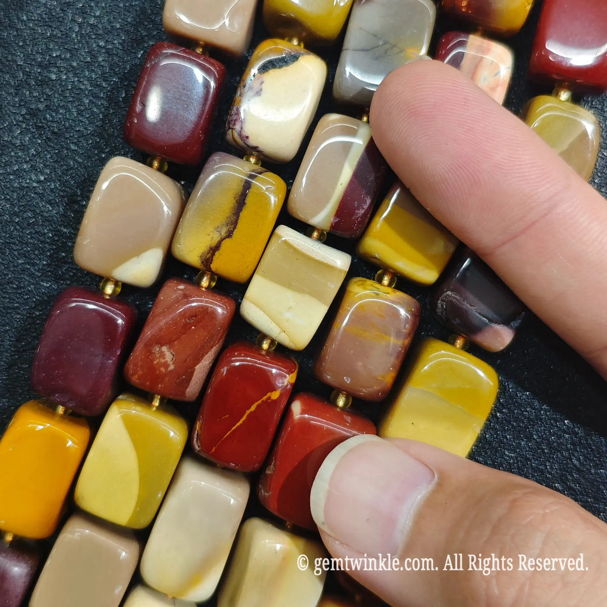 Finger inspecting Mookaite Jasper square column beads highlighting uniform shape and smooth polished edges
