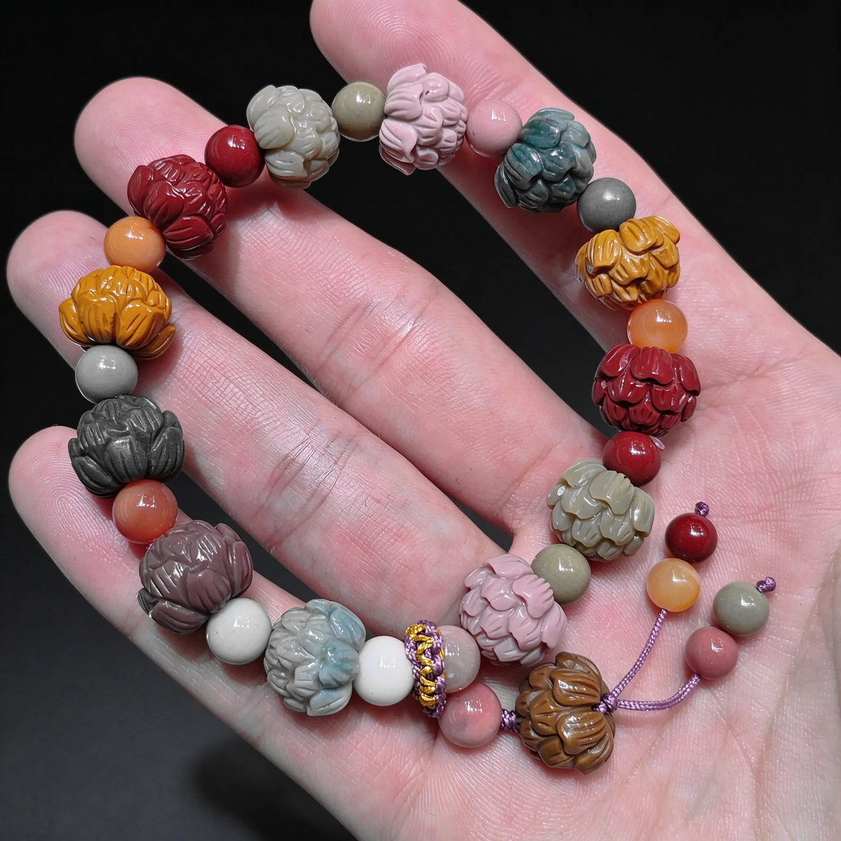 Palm displaying a natural multi color Alxa agate carved lotus bead bracelet featuring red yellow green and pink lotus carved beads