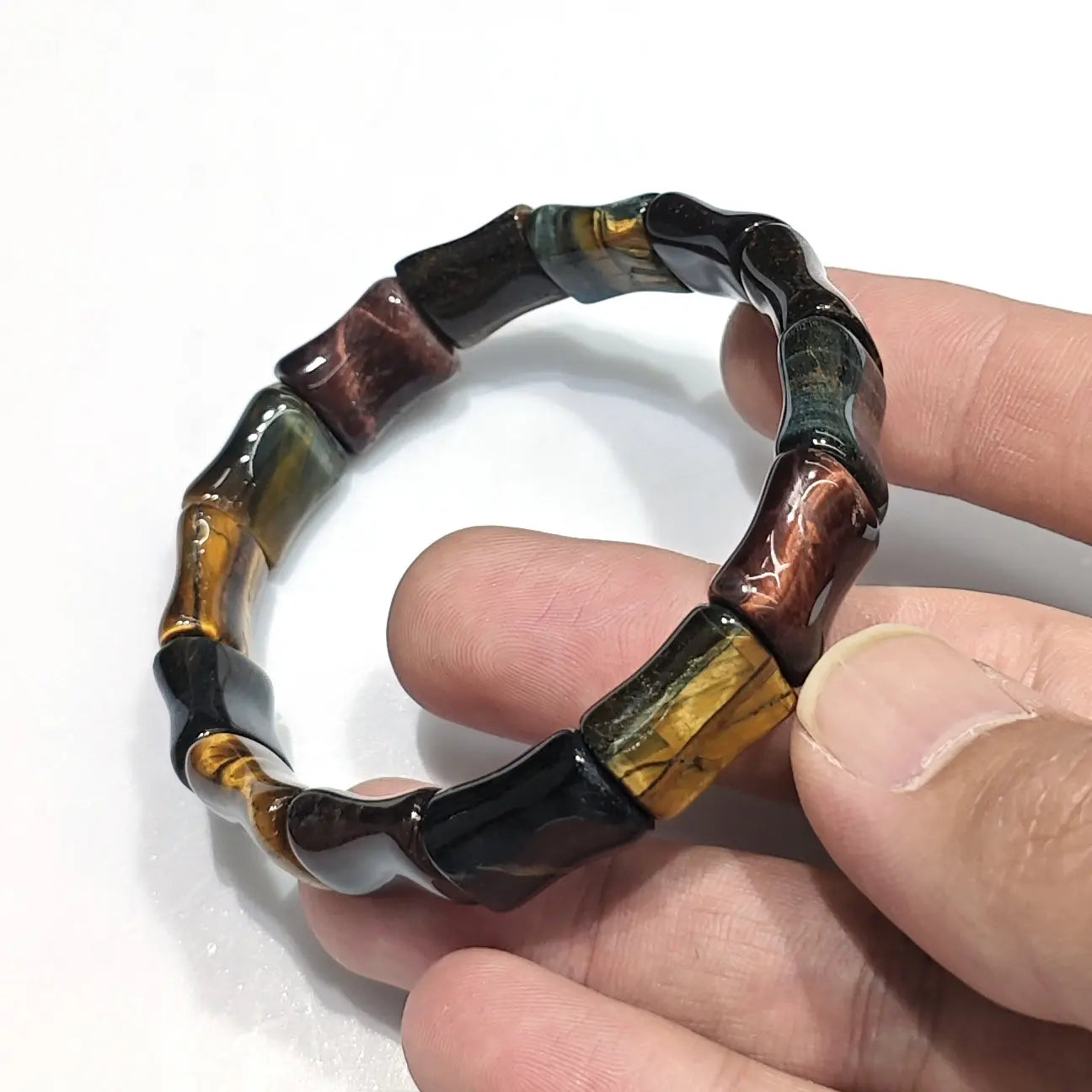 Hand holding natural multicolor tiger eye elastic bracelet with bamboo-shaped beads (15mm units), showing yellow, blue, and red bands — fits standard 18cm wrist, unisex design