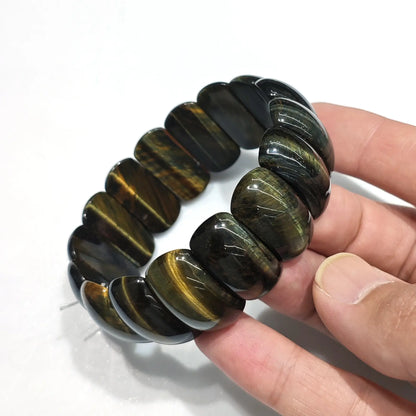 Hand holding natural multicolor tiger eye elastic bracelet with 25mm beads (red, yellow, blue, black bands), displayed on 18cm wrist — unisex fit for wholesale resale